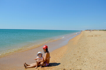 Mom and baby sit on a sandy beach near the black sea on a clear, Sunny day.