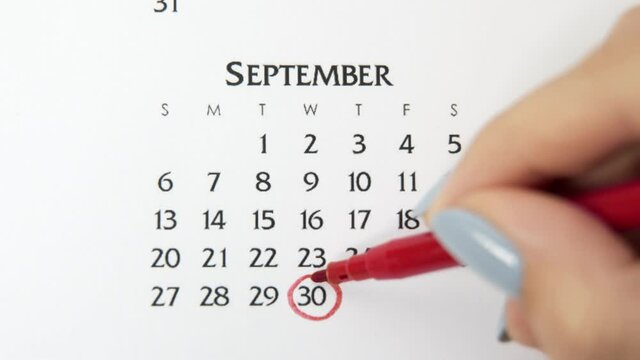 Female hand circle day in calendar date with a red marker. Business Basics Wall Calendar Planner and Organizer. September 30th