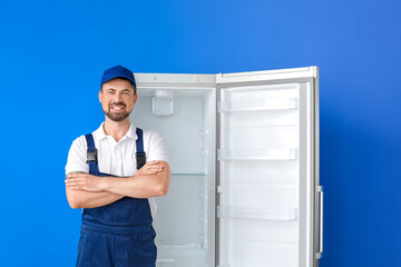 Worker of repair service near fridge on color background