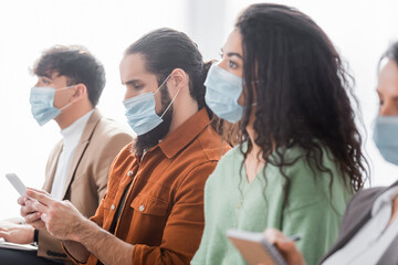 man using smartphone during business lection near hispanic colleagues in medical masks