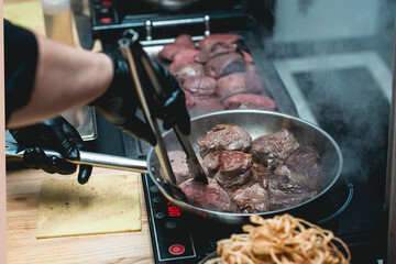 Close-up of chef in gloves prepares steak in a frying pan