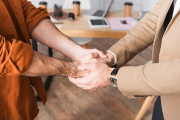 cropped view of hispanic businesspeople shaking hands in office on blurred background