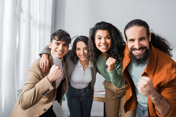 happy hispanic businesspeople embracing, looking at camera and showing winner gesture