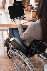 back view of handicapped hispanic businesswoman using laptop with blank screen during meeting