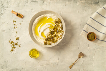Popular middle eastern appetizer labneh or labaneh, soft white goat milk cheese with olive oil, hyssop or zaatar, served with pita bread over grey table, flaylay.