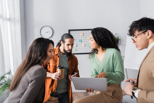 Hispanic office workers looking at laptop in hands of female colleague during break at workplace