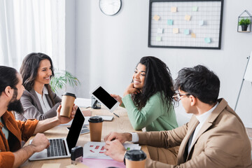 Fototapeta premium Smiling hispanic office workers talking, while sitting at workplace with devices in office
