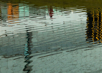 Abstract reflection in the water. Sunny day. Distorted view with ripples. Urban shot. Building windows in reflection.