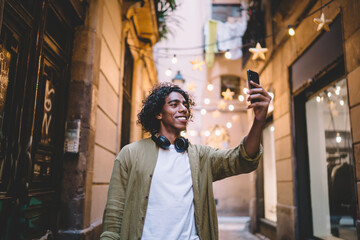 Cheerful young tourist taking selfie against entrance of building