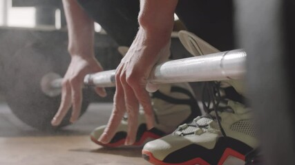 Close up low section shot of unrecognizable woman in sportswear applying powder chalk to palms and taking barbell while training in gym