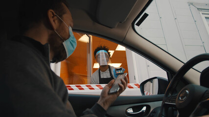 Man driver in mask paying with smartphone app in drive through window