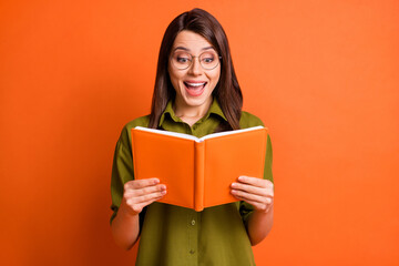 Photo portrait of amazed happy female student wearing eyewear reading book smiling isolated on vivid orange color background