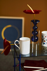 Stylish compositon at modern living room interior with design coffee table, mug, book and red flower. Close up. Yellow wall. Template.