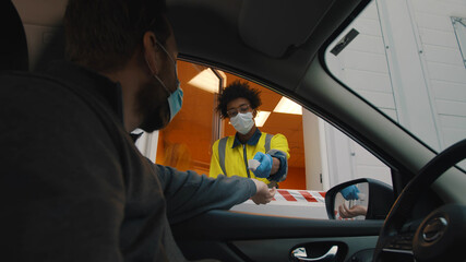 Man driver in safety mask stopping near security booth for temperature scanning before entering area