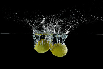 close up view of fresh lemon citrus fruit falling into water isolated on black background