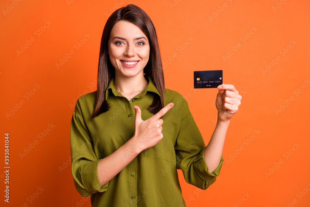 Sticker Photo portrait of young girl pointing at bank plastic card isolated on bright orange color background