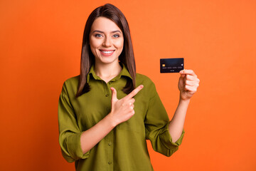 Photo portrait of young girl pointing at bank plastic card isolated on bright orange color background