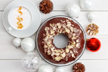 Homemade chocolate cheesecake with almond slices, cup of coffee cappuccino and Christmas balls on white wooden table. Top view.