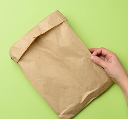 two hands holding a paper bag of brown kraft paper ona green background