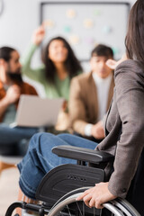 lecturer in wheelchair pointing with hand at hispanic woman having question on blurred background