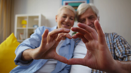 Cheerful senior couple making heart shape with their hands and fingers at home