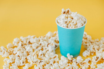 Popcorn in a blue paper cup on a yellow background. Minimalist concept. Copy, empty space for text