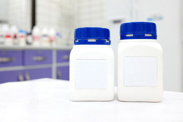 Two unlabeled plastic chemical bottle container with cap in a white chemistry laboratory with copy space. 