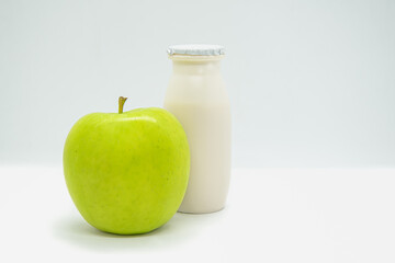 Natural liquid yogurt with prebiotics in small plastic bottle and green apple on white background. Healthy, balanced diet food, healthy breakfast. Space for text.