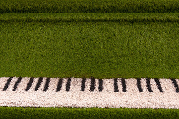 Green sculpture of grand piano with real white and black keyboard made from artificial grass. Urban.