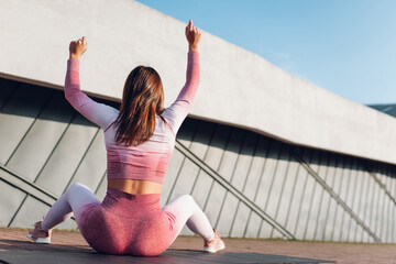 Athletic girl sitting on yoga mat with raised arms and celebrating victory