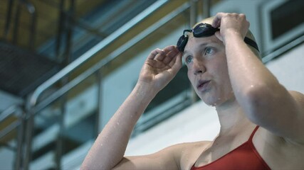 Woman athlete nervously take a deep breath, focus to start swimming, put her goggles on and prepare to jump to the pool. Slow motion video. Top shot. 