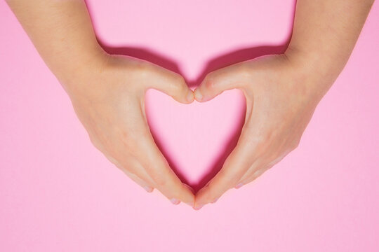 Close-up of a woman's hands drawing a heart on a pink background. Love and Valentine concept.