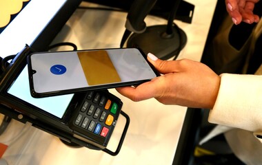 A young woman pays for purchases with her smartphone via the app.The terminal for payment.Using your smartphone to pay for purchases. Contactless payment.Accept payment by NFC technology in a retail 