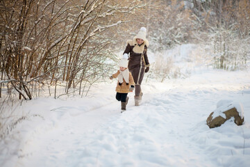 mother and daughter in brown fur coats walk through the winter forest. lots of snow around.
