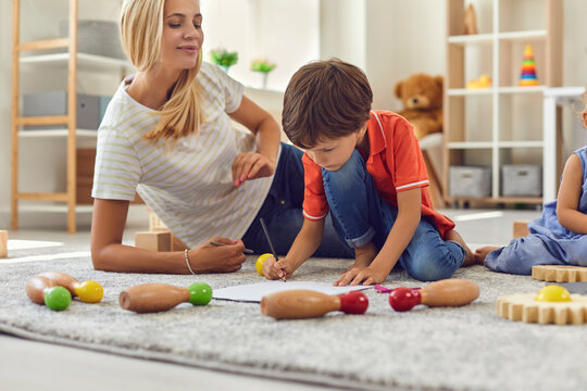 Mother sitting on floor carpet with children and drawing together at home