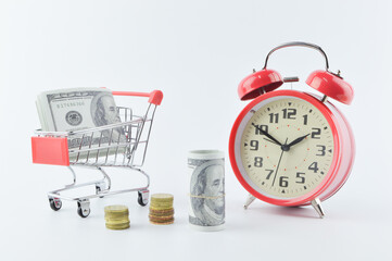 View of alarm clock, banknotes, coins and shopping cart isolated on a white background. Shopping concept.