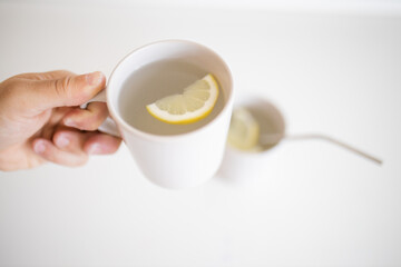 Hand holding a cup of lemon tea with a lemon slice inside