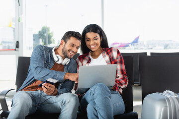happy interracial couple looking at laptop in airport