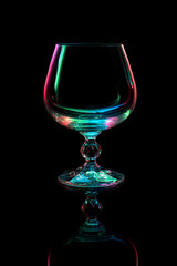 Cognac glass silhouette. Multi-colored iridescent light on a black background with reflection. 