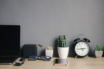 Alarm clock and plants on white pot with office and personal accessories on work table and grey background. Minimalist office interior concept
