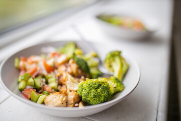 Broccoli and chicken salad on white bowl next to a window