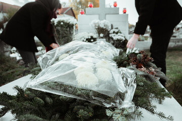 A women and a man putting flowers on a grave on All soul's day in a vblack coat.