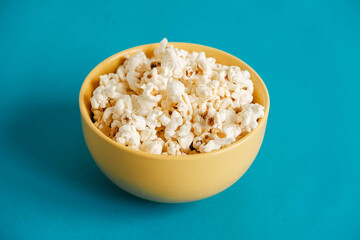 Popcorn in a yellow bowl on a blue background. Copy, empty space for text
