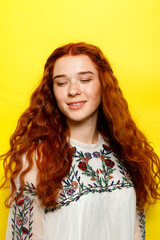 Indoor portrait of excited curly woman with trendy makeup. Ginger caucasian young lady smiling on yellow background. redhead girl with flying curly hair smiling laughing