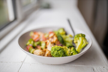 Broccoli and chicken salad on white bowl next to a window