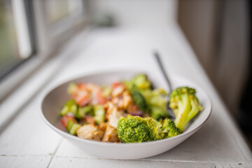 Broccoli and chicken salad on white bowl next to a window