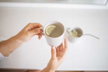 Hands holding a cup of lemon tea with a lemon slice inside