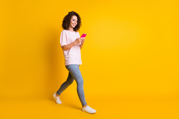 Fototapeta na wymiar Full length body size photo of female millennial using app mobile phone walking isolated on vibrant yellow color background with copyspace