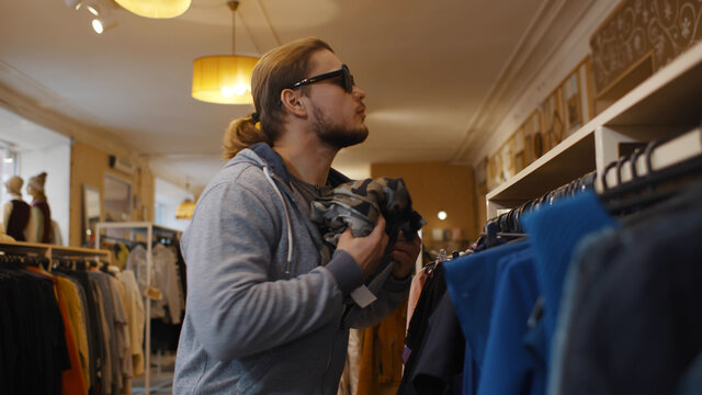 Young man in sunglasses hiding jeans in jacket at clothes store