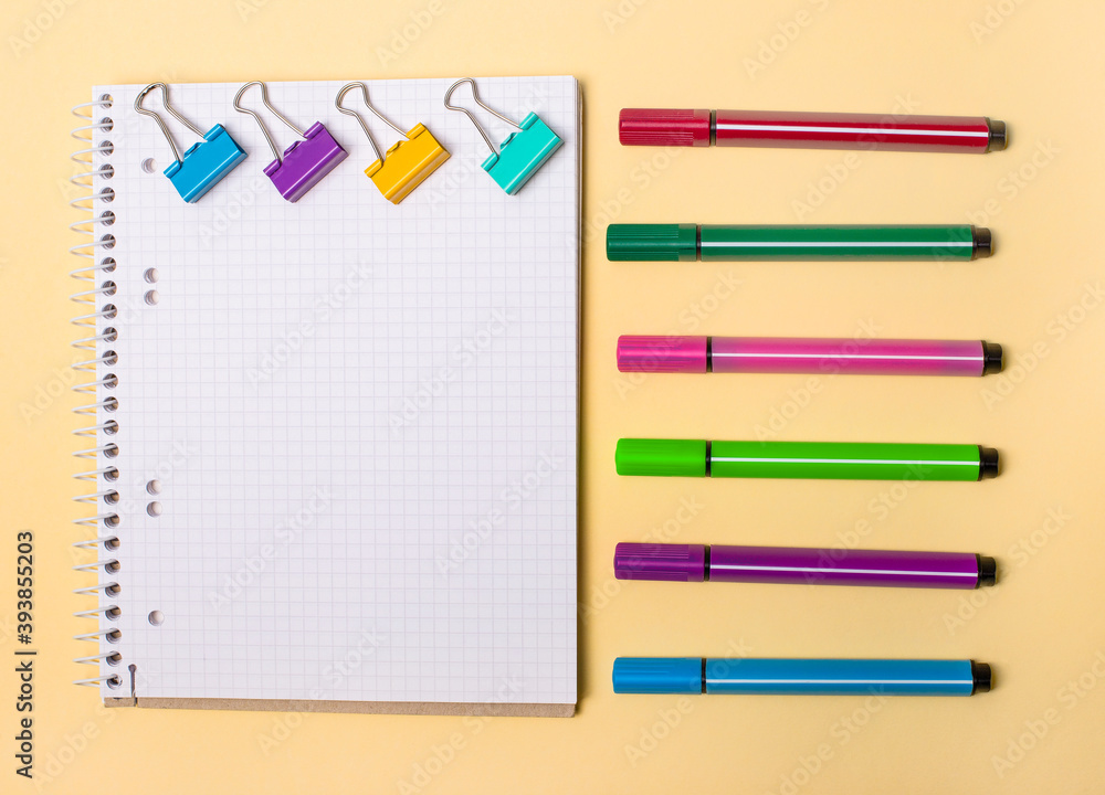 Poster on a beige background there is a blank notebook, colored paper clips and various colored markers. pl